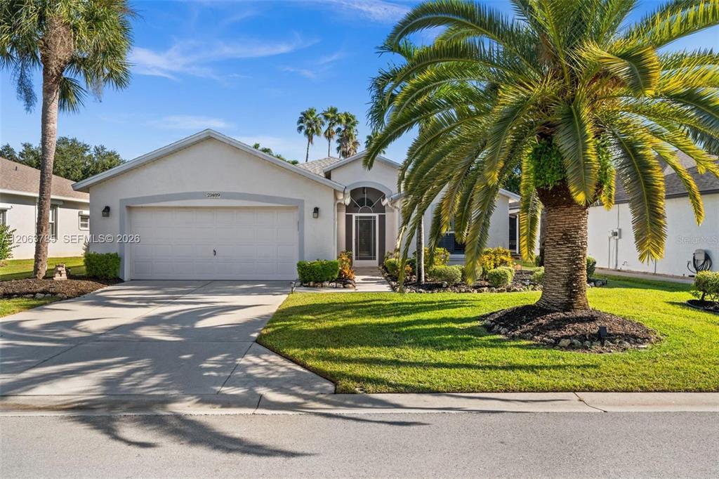 A single-story house with a white stucco exterior, a two-car garage, and a large palm tree — 21489 SHERIDAN RUN, ESTERO, FL