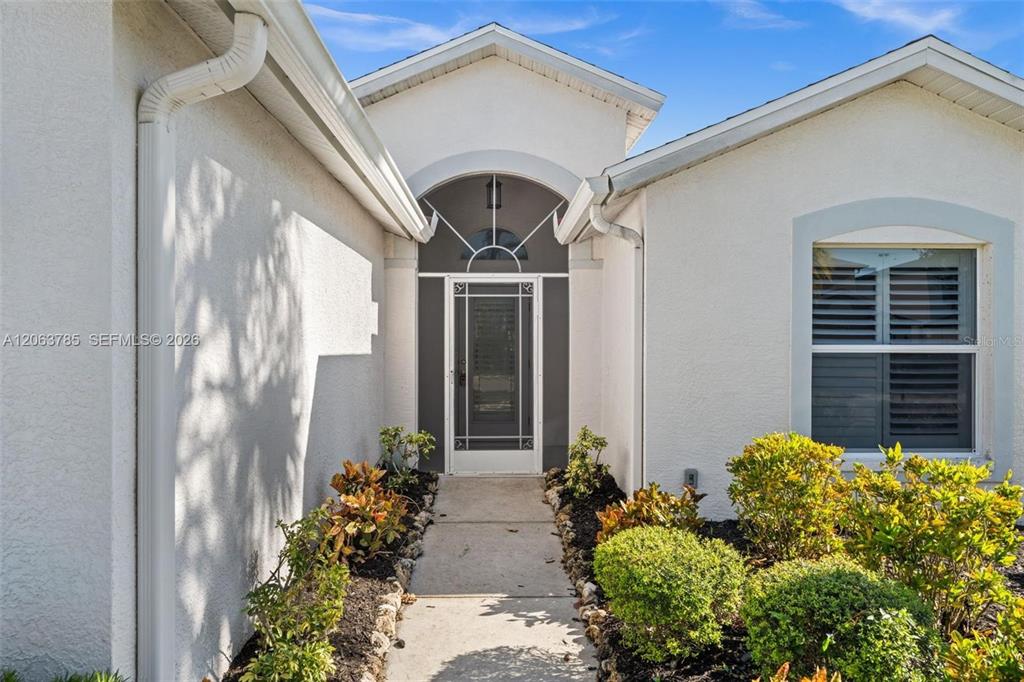 The exterior view shows a white stucco house entrance with a glass door and landscaping — 21489 SHERIDAN RUN, ESTERO, FL