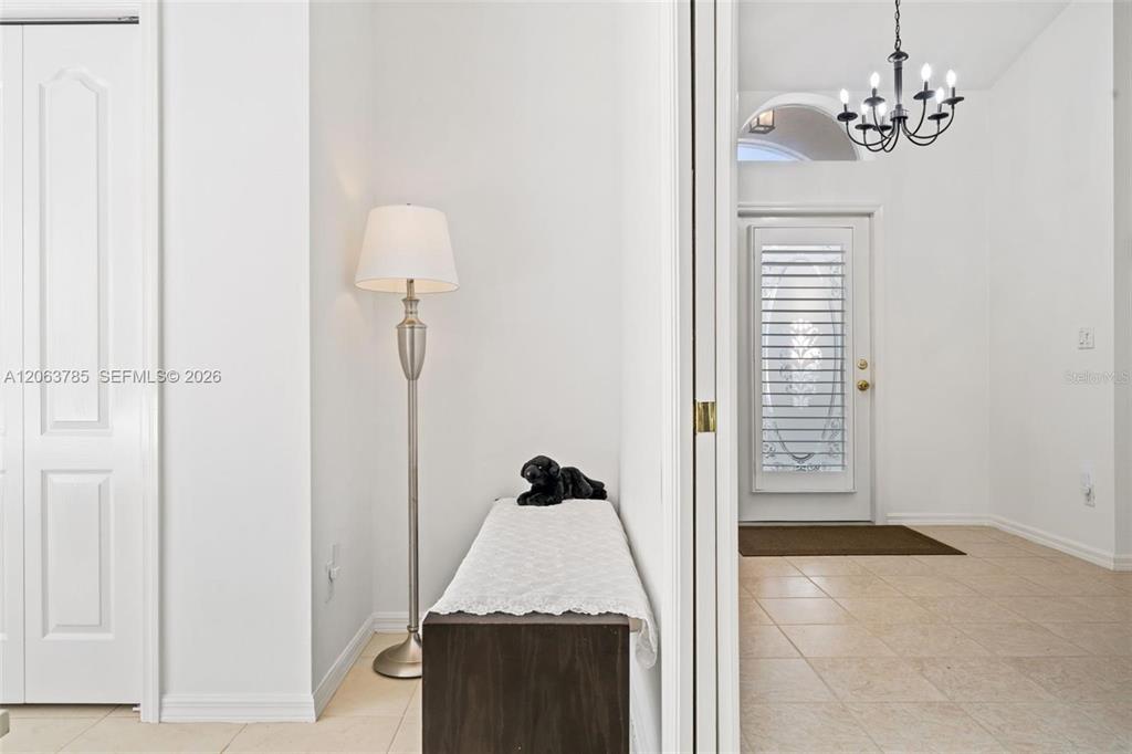 An entryway features a white door, a floor lamp, a bench, and a chandelier — 21489 SHERIDAN RUN, ESTERO, FL