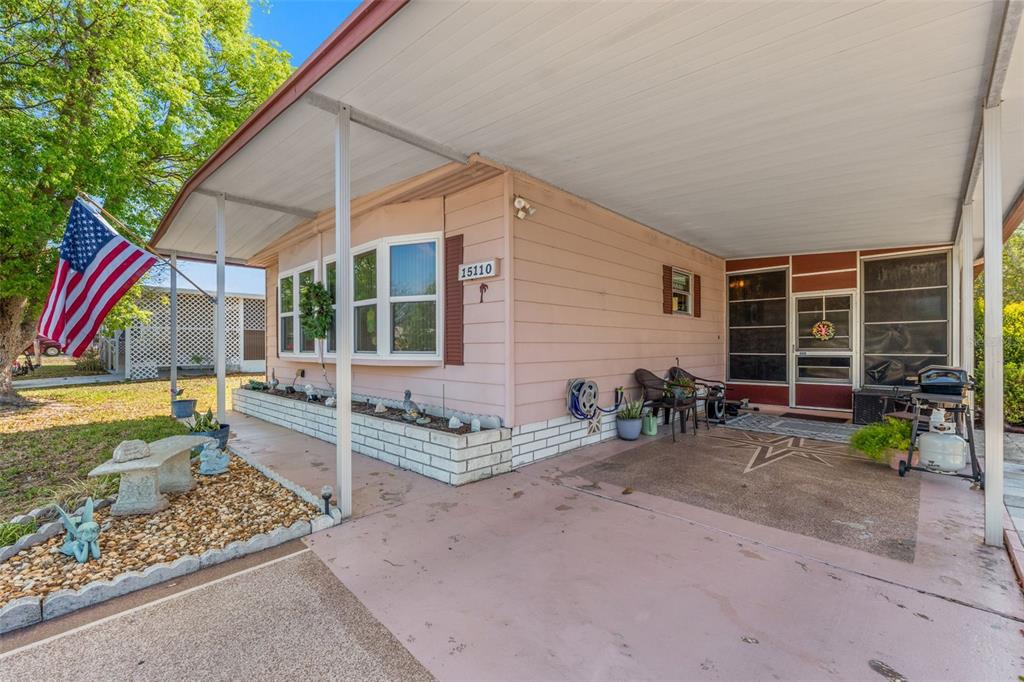 A pink mobile home features a covered carport, a front porch, and a small garden bed — 15110 RIALTO AVENUE, BROOKSVILLE, FL