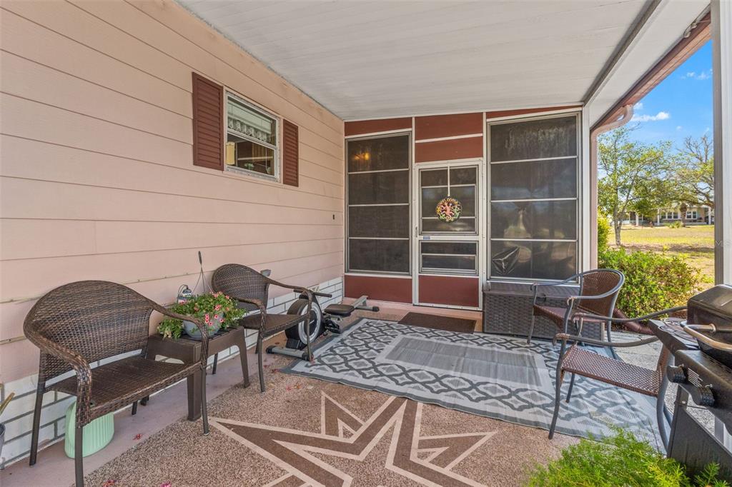 A covered patio features wicker chairs, a patterned rug, and a screen door entrance — 15110 RIALTO AVENUE, BROOKSVILLE, FL