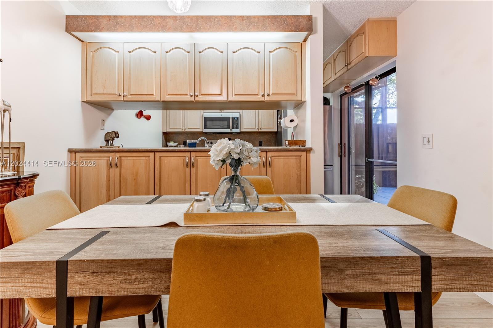 A dining area with a wooden table and yellow chairs faces a kitchen with light-wood cabinets — 9135 SW 20th Pl, Davie FL 33324, DAVIE, FL