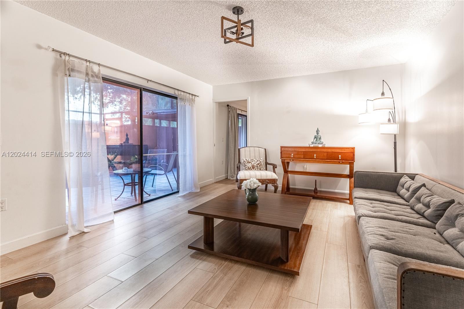 A living room features light wood-look flooring, a gray sofa, and a sliding glass door — 9135 SW 20th Pl, Davie FL 33324, DAVIE, FL