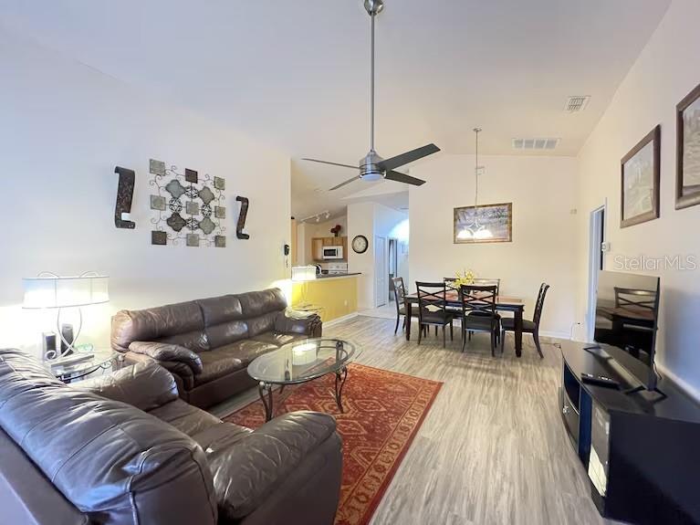 A living room with a brown leather sofa, dining area, and light wood-look flooring — 136 STARBIRD COURT, DAVENPORT, FL