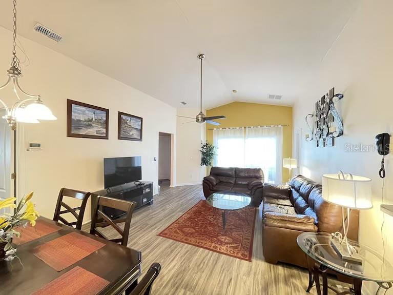 A living room and dining area feature wood-look flooring, vaulted ceilings, and a ceiling fan — 136 STARBIRD COURT, DAVENPORT, FL