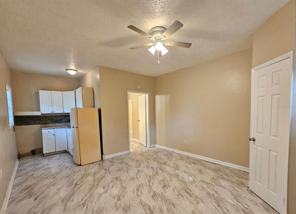 A kitchen and living area with tan walls, white cabinets, and light-colored marble-patterned tile flooring — 1504 E 99TH AVENUE UNIT C, TAMPA, FL