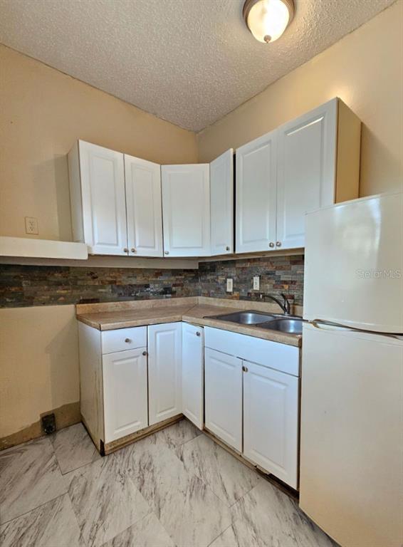 A kitchen features white cabinets, a stone tile backsplash, laminate countertops, and a white refrigerator — 1504 E 99TH AVENUE UNIT C, TAMPA, FL
