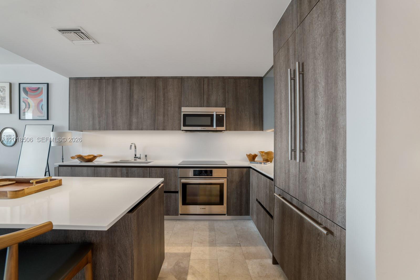 A modern kitchen features dark wood cabinetry, stainless steel appliances, and a white island countertop — 88 SW 7th St # 2406, Miami FL 33130, MIAMI, FL
