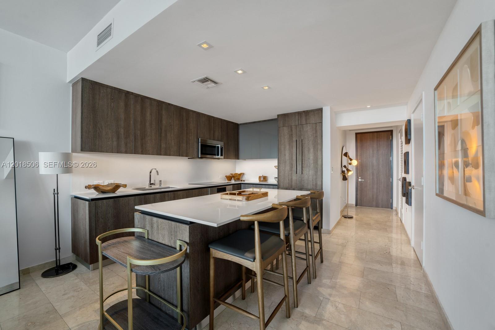 A modern kitchen features dark wood cabinetry, a white island, and marble tile flooring — 88 SW 7th St # 2406, Miami FL 33130, MIAMI, FL