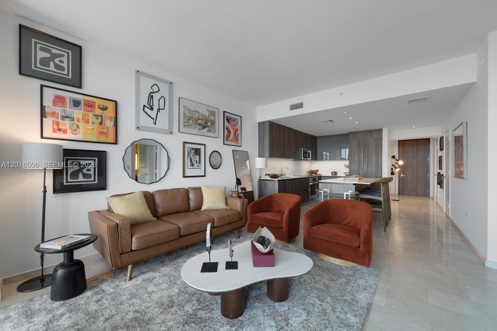 A living room with a brown leather sofa, two orange chairs, and a kitchen area — 88 SW 7th St # 2406, Miami FL 33130, MIAMI, FL