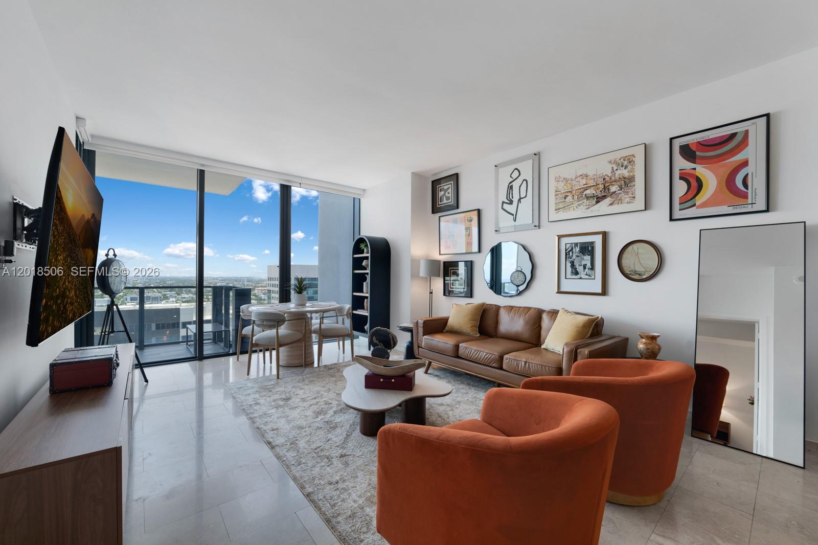 A modern living room features a brown leather sofa, orange armchairs, and floor-to-ceiling windows — 88 SW 7th St # 2406, Miami FL 33130, MIAMI, FL