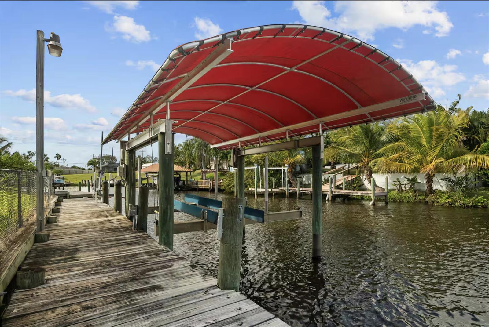 A wooden boat dock features a large red canopy covering a mechanical boat lift — PORT ST. LUCIE, FL
