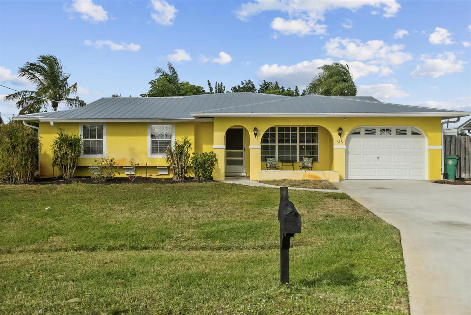 A yellow single-story house features a metal roof, an arched porch, and a garage — PORT ST. LUCIE, FL