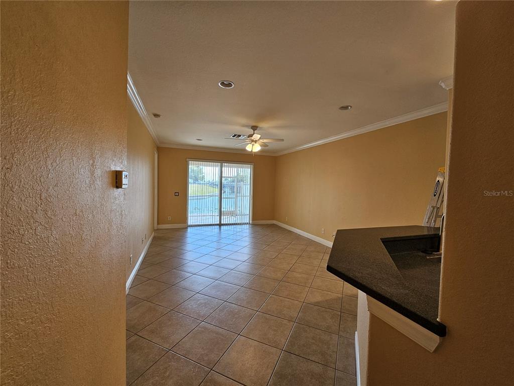 An empty living room features tan walls, tile flooring, a ceiling fan, and sliding glass doors — 231 CULTURAL PARK BOULEVARD S UNIT B, CAPE CORAL, FL