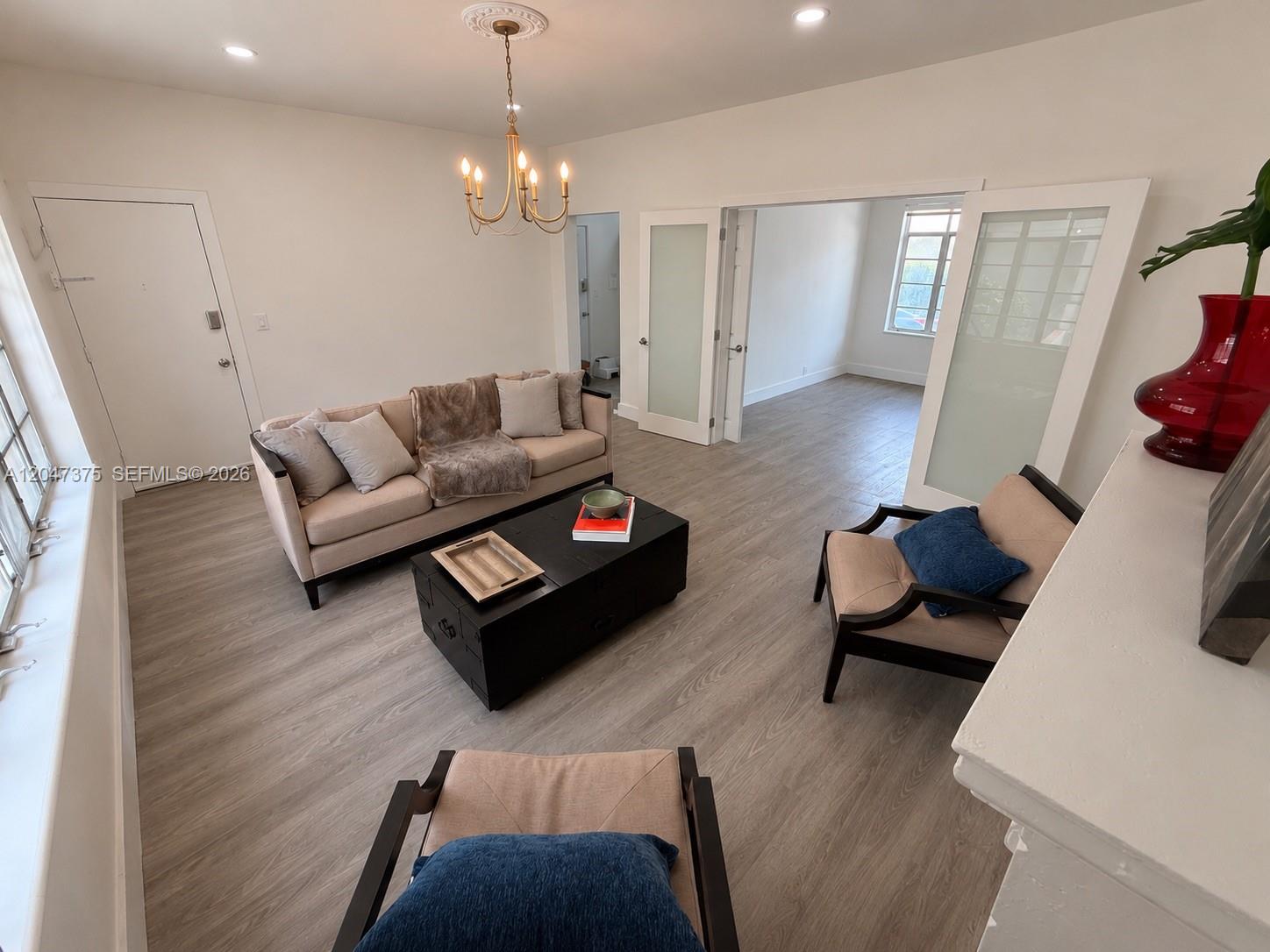 A living room features light wood-look flooring, a beige sofa, two armchairs, and a chandelier — 762 Lenox Ave # 2, Miami Beach FL 33139, MIAMI BEACH, FL