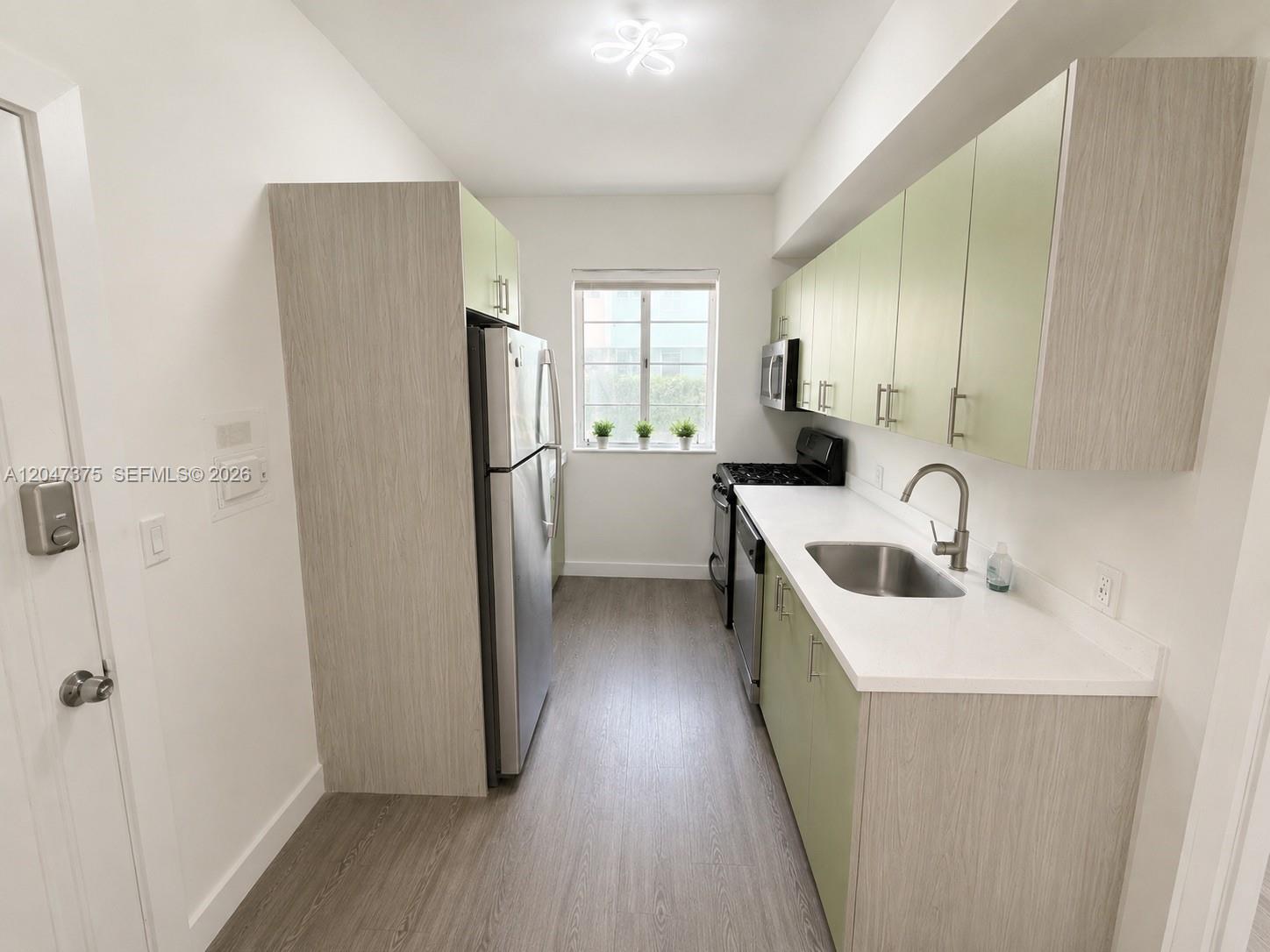 This galley kitchen features light green cabinets, stainless steel appliances, and white countertops — 762 Lenox Ave # 2, Miami Beach FL 33139, MIAMI BEACH, FL