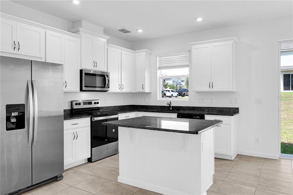 A kitchen with white cabinets, dark granite countertops, stainless steel appliances, and a center island — 1100 LAKESHORE BREEZE PLACE, KISSIMMEE, FL