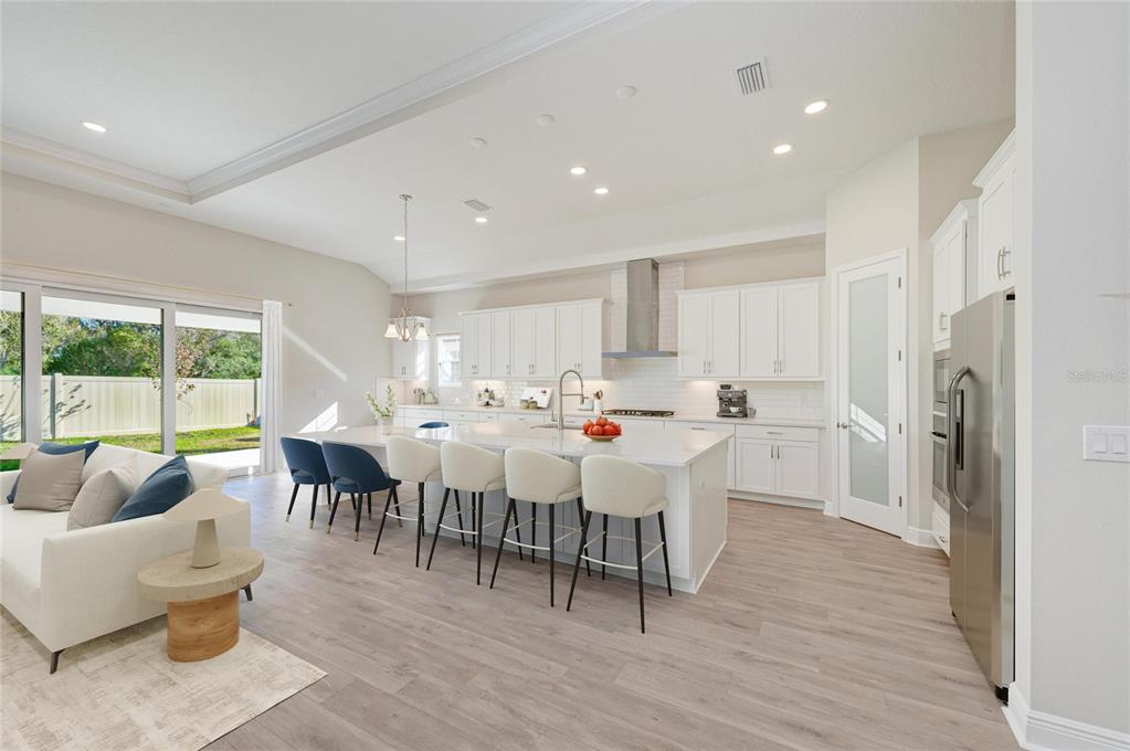 A modern open-concept kitchen features white cabinetry, a large island with seating, and light flooring — 13068 HOMESTEAD LANE, PARRISH, FL