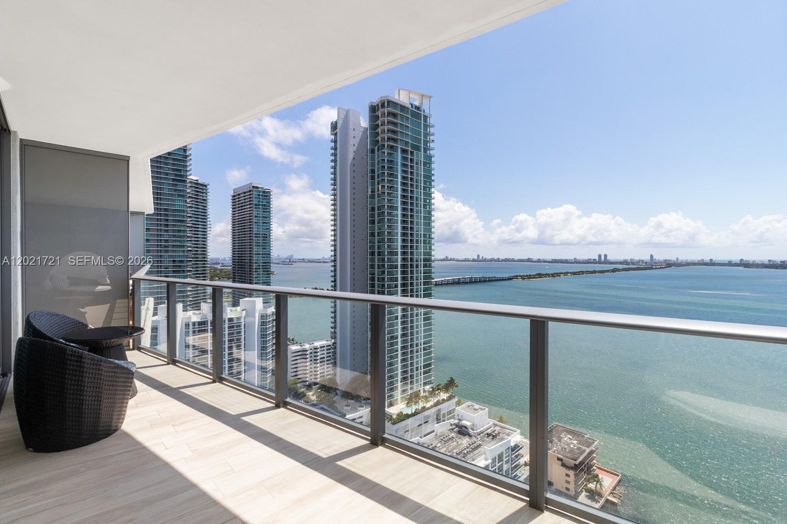 A balcony with outdoor seating overlooks a bay, a bridge, and several high-rise buildings — 460 NE 28th St # 3105, Miami FL 33137, MIAMI, FL
