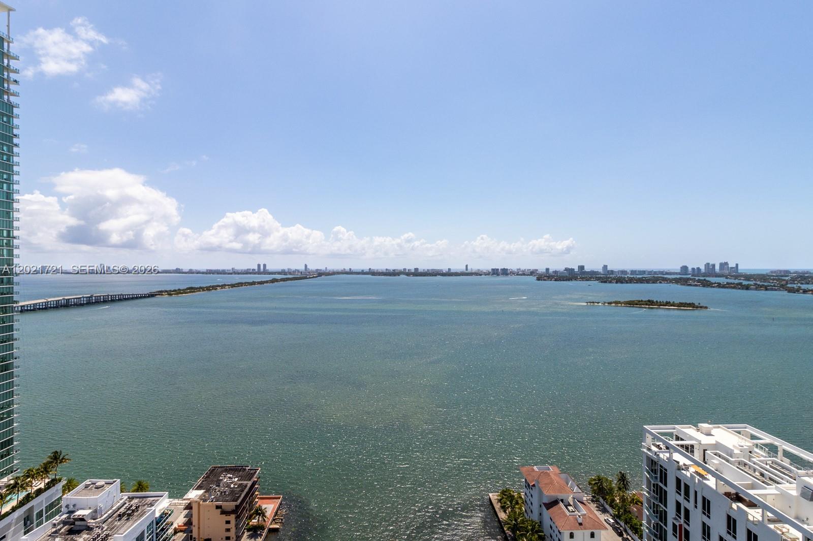 An elevated view of a bay with a bridge, distant city skyline, and surrounding buildings — 460 NE 28th St # 3105, Miami FL 33137, MIAMI, FL