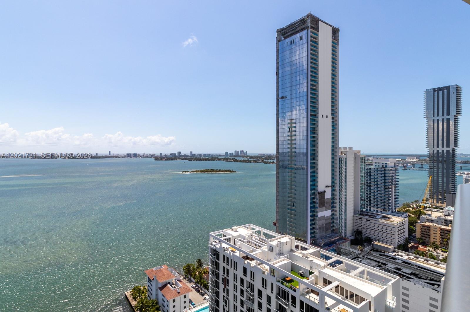An elevated view shows a modern glass skyscraper overlooking a bay with a small island — 460 NE 28th St # 3105, Miami FL 33137, MIAMI, FL