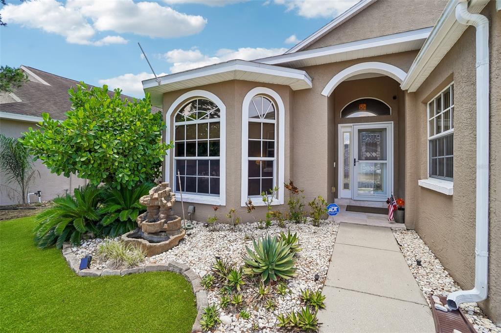 The exterior of a tan house features a stone fountain, rock landscaping, and arched windows — 1817 WOOD BEND STREET, TARPON SPRINGS, FL