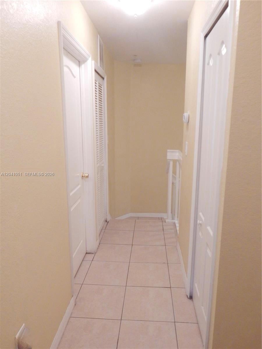 A tiled hallway features white doors and a staircase railing leading to another level — 8826 W Flagler St # 203, Miami FL 33174, MIAMI, FL