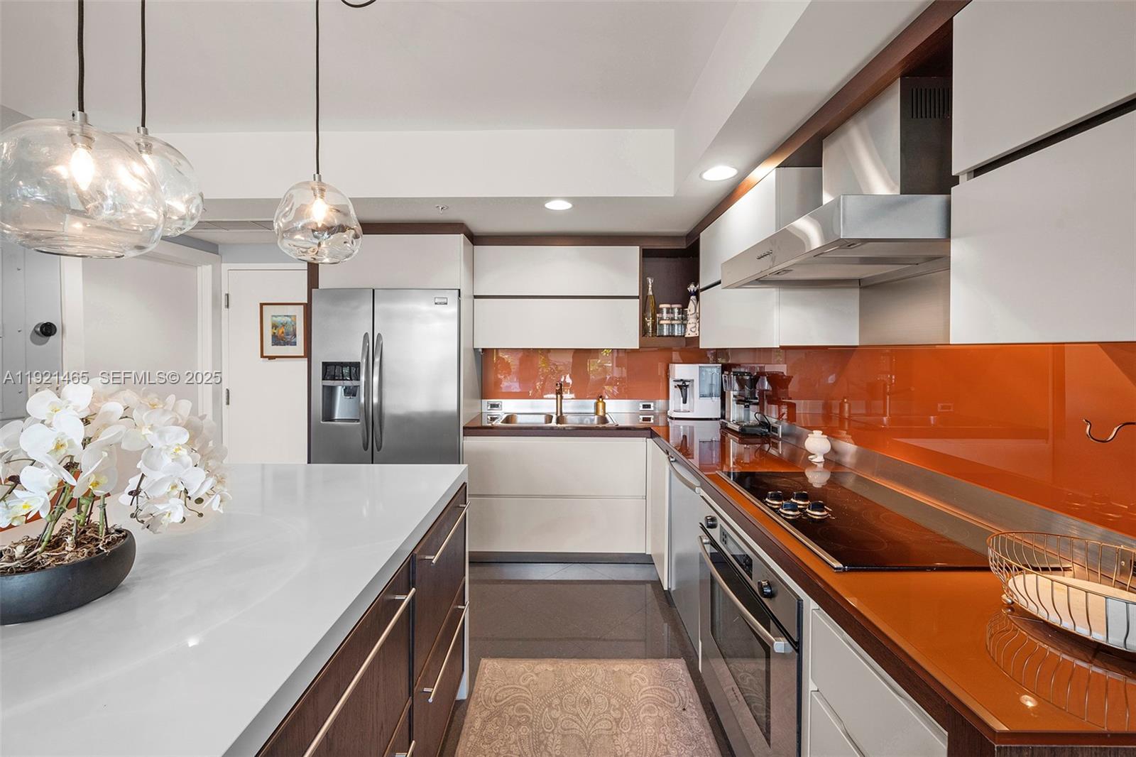 A modern kitchen features white cabinetry, a large island, stainless steel appliances, and orange backsplashes — 2155 Washington Ct # 205, Miami Beach FL 33139, MIAMI BEACH, FL