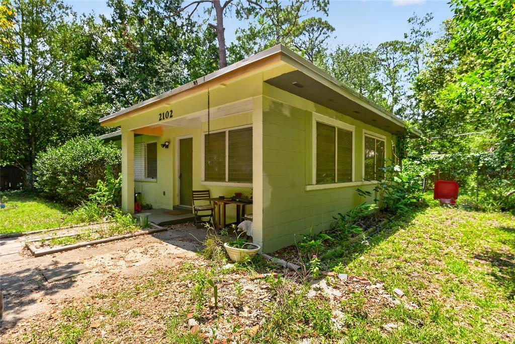 A small, light green house with a covered porch sits in a wooded yard — 2102 NE 8TH STREET, GAINESVILLE, FL