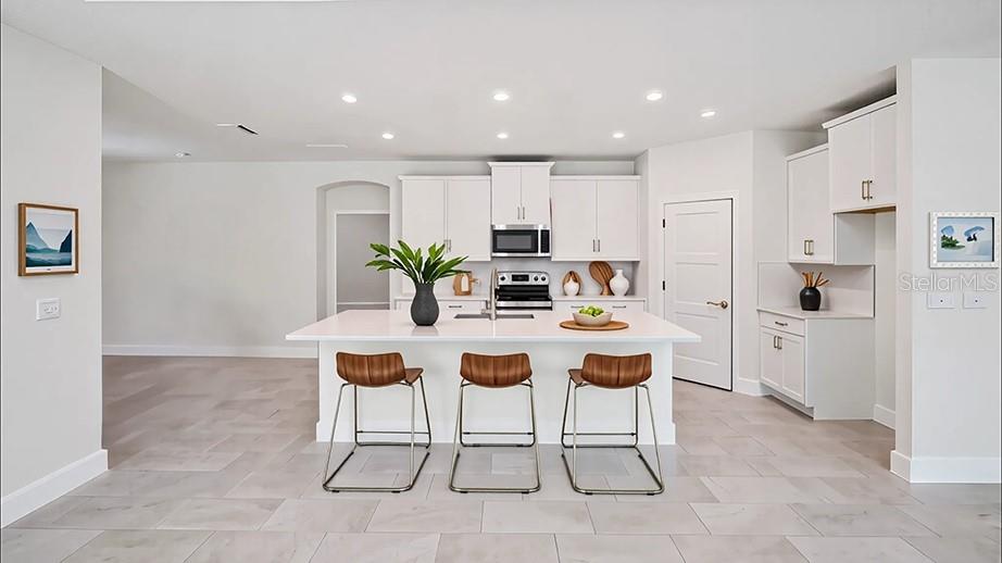 A modern white kitchen features a central island with three stools and light tile flooring — 11389 CURIO DRIVE, BROOKSVILLE, FL