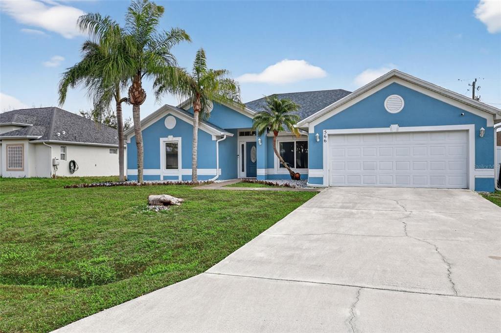 A blue single-story house with a two-car garage, palm trees, and a concrete driveway — 566 SW SEA HOLLY TERRACE, PORT ST LUCIE, FL