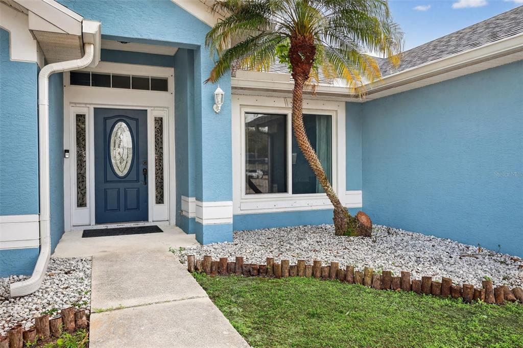 The exterior of a blue house features a front door with glass inlay and a palm tree — 566 SW SEA HOLLY TERRACE, PORT ST LUCIE, FL