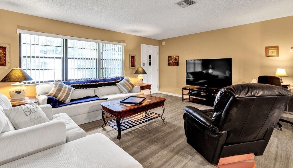 A living room features a white sofa, a black leather recliner, and wood-look flooring — SEBASTIAN, FL