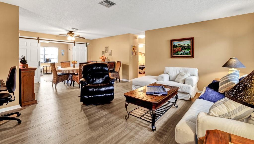 A living room with wood-look flooring, a white sofa, a black recliner, and a dining area — SEBASTIAN, FL