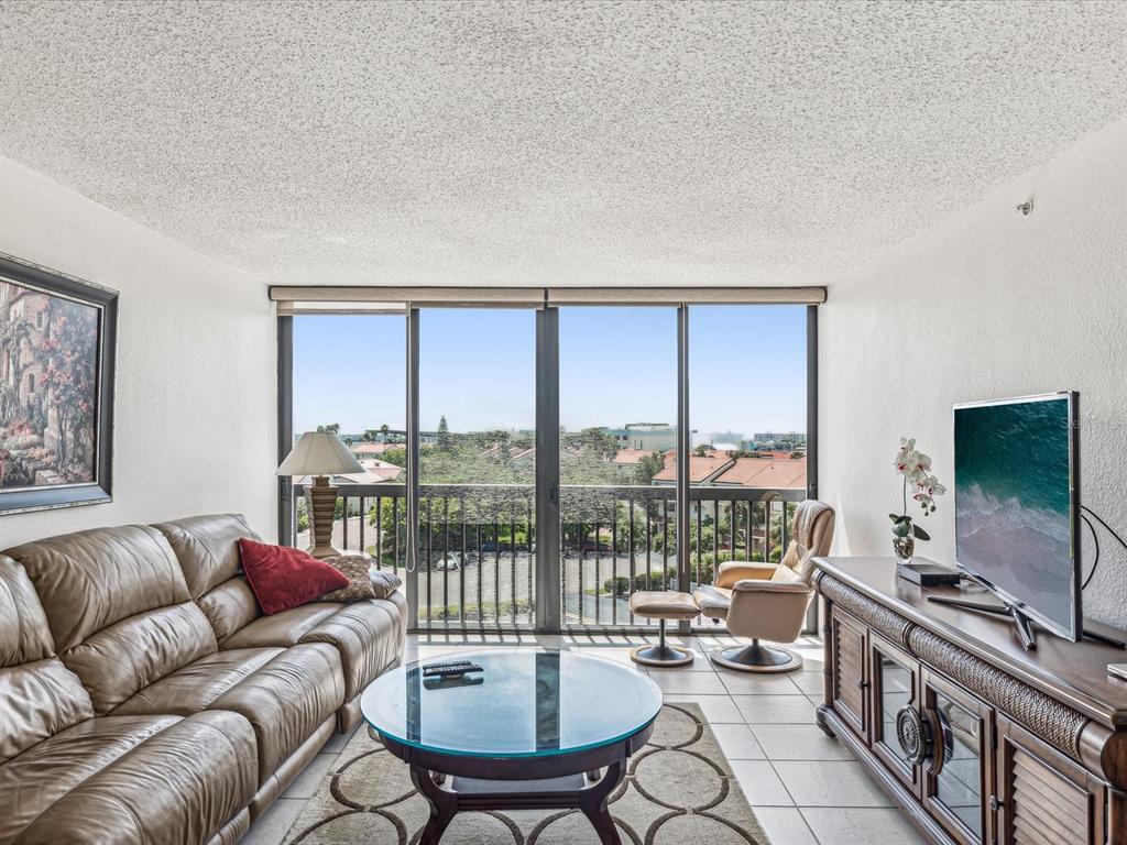 A living room features a leather sofa, glass coffee table, and sliding doors to a balcony — 255 DOLPHIN POINT UNIT 501, CLEARWATER BEACH, FL