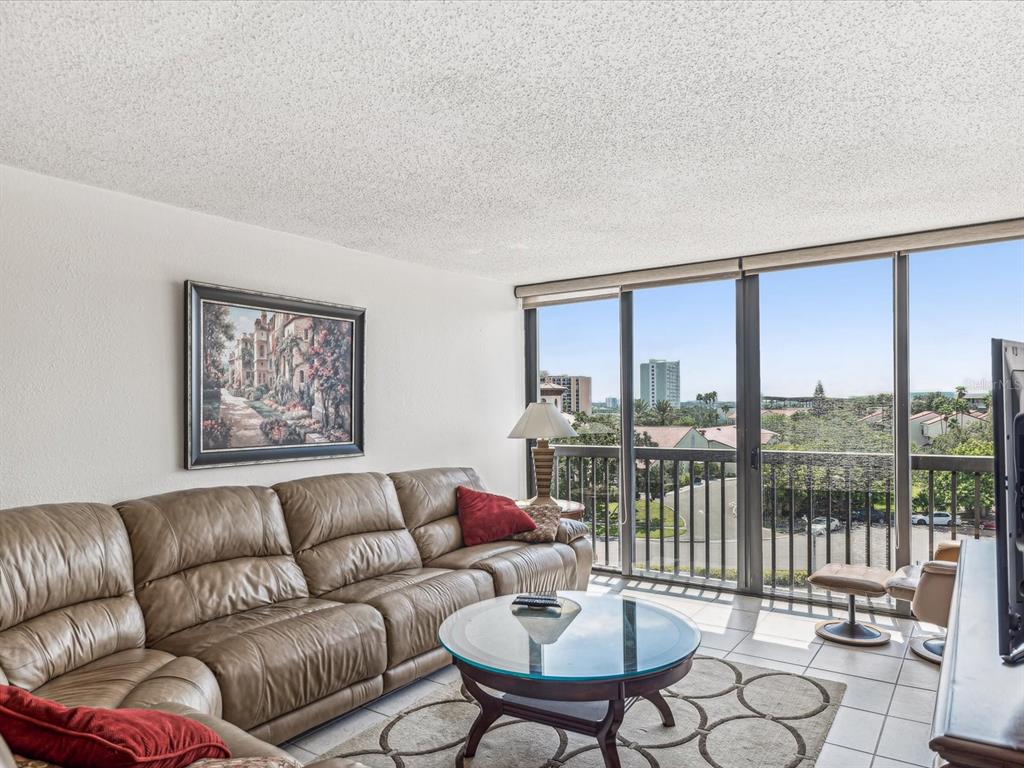 A living room with a leather sectional, glass coffee table, and floor-to-ceiling windows with views — 255 DOLPHIN POINT UNIT 501, CLEARWATER BEACH, FL
