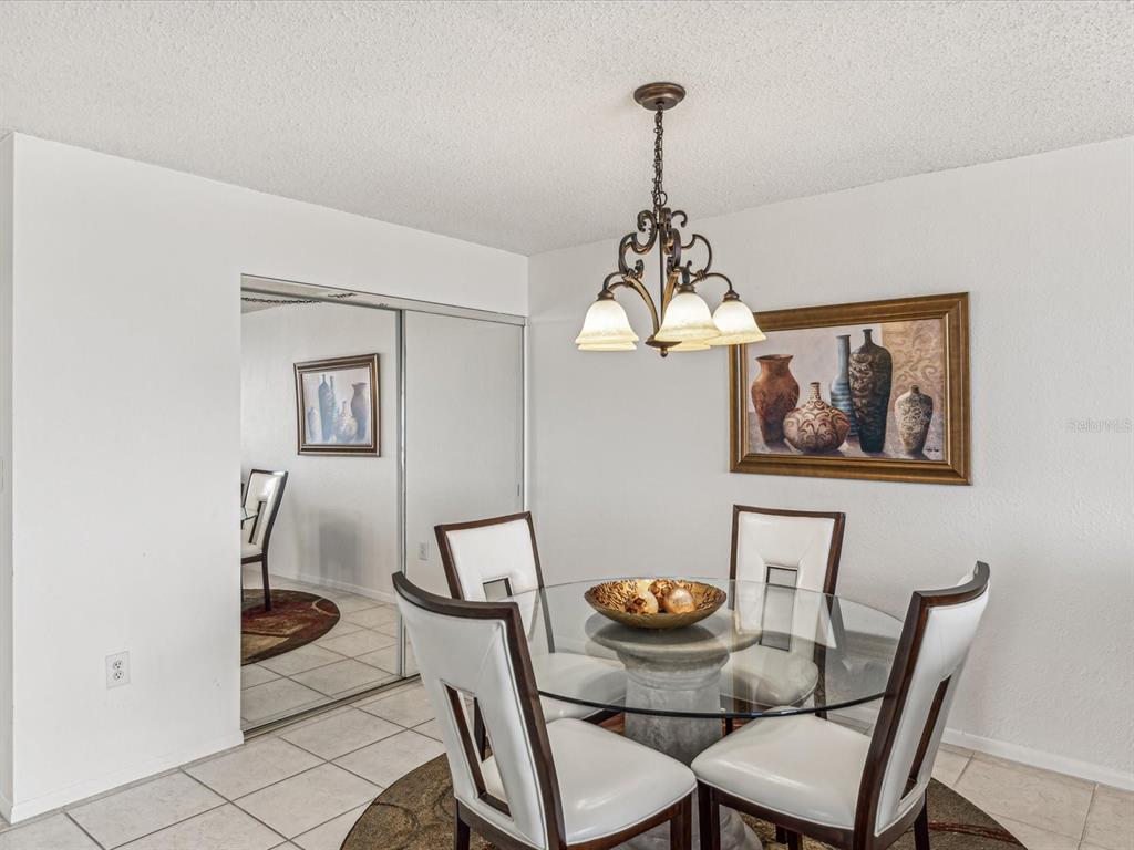 A dining area features a glass-topped table, four chairs, a chandelier, and mirrored closet doors — 255 DOLPHIN POINT UNIT 501, CLEARWATER BEACH, FL
