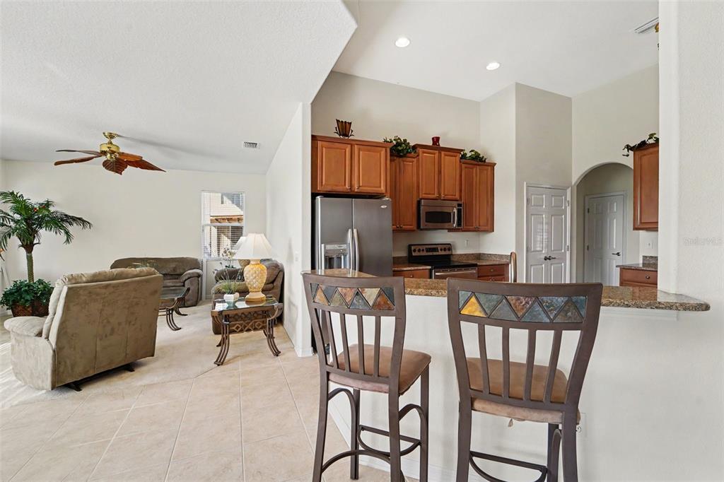 A kitchen with wood cabinets and stainless appliances overlooks a living area with tile flooring — 1316 BLUE MARLIN BOULEVARD, HOLIDAY, FL