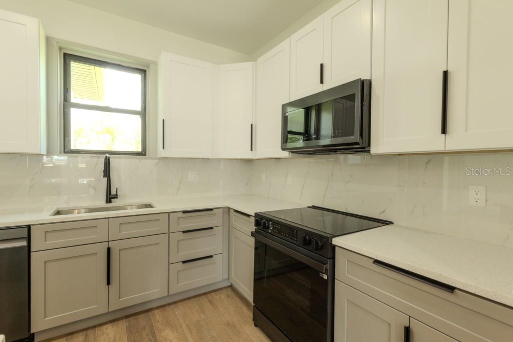 A kitchen with white upper cabinets, gray lower cabinets, black appliances, and a marble backsplash — 5438 SYLVANIA AVENUE, NORTH PORT, FL