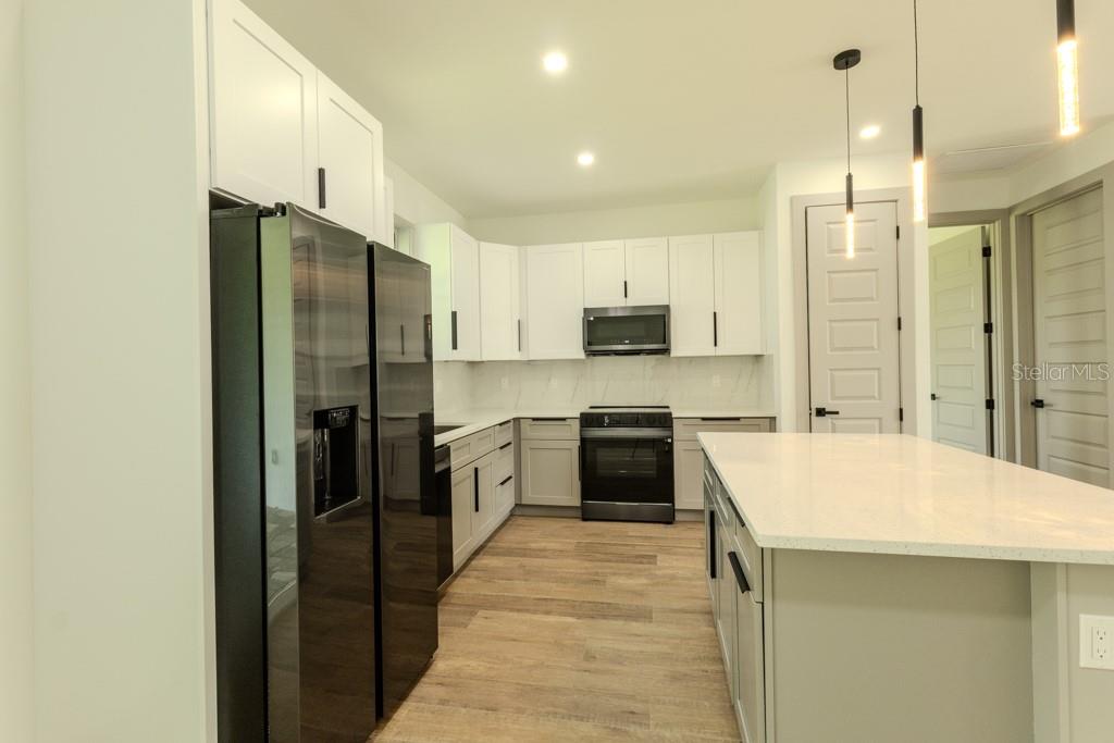A modern kitchen features white cabinets, stainless steel appliances, and a large central island — 5438 SYLVANIA AVENUE, NORTH PORT, FL