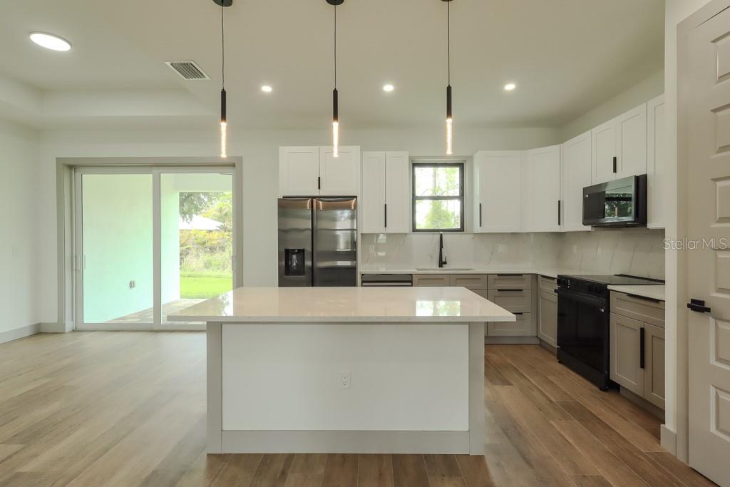A modern kitchen features white upper cabinets, gray lower cabinets, a central island, and stainless appliances — 5438 SYLVANIA AVENUE, NORTH PORT, FL