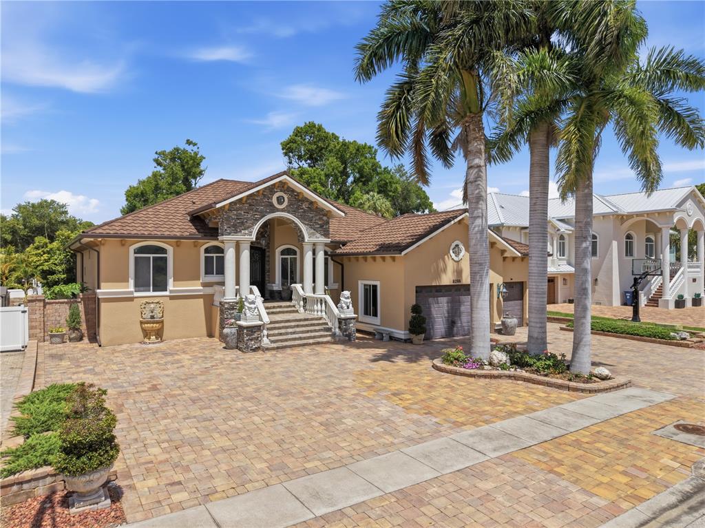 A tan house with a stone-accented arched entryway, a paver driveway, and tall palm trees — 8286 N 97TH N ST, SEMINOLE, FL