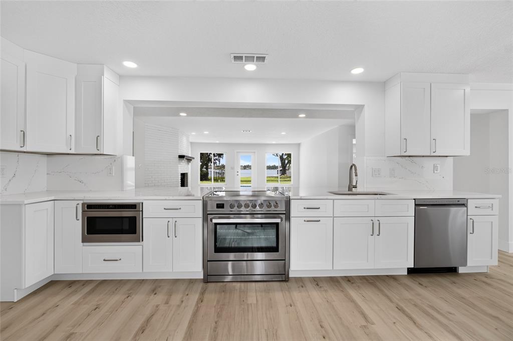 A modern kitchen features white cabinetry, stainless steel appliances, and light wood-look flooring — 1225 HOFFNER AVENUE, ORLANDO, FL