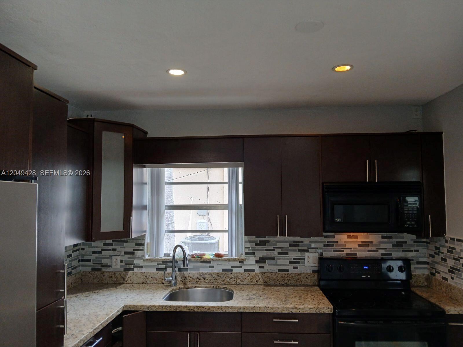 A kitchen features dark wood cabinets, granite countertops, a mosaic tile backsplash, and stainless appliances — 2111 N 57th Terrace, Hollywood FL 33021, HOLLYWOOD, FL