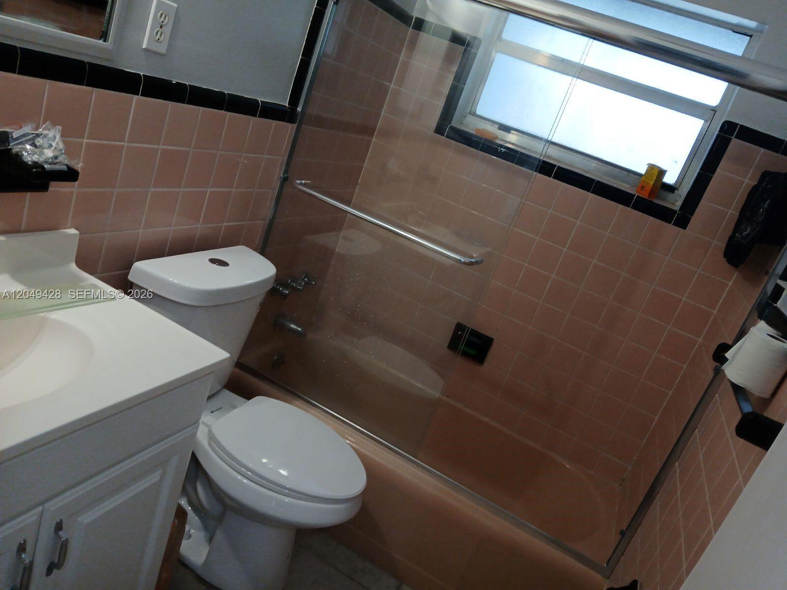 A bathroom features a white vanity, a toilet, and a pink-tiled shower with glass doors — 2111 N 57th Terrace, Hollywood FL 33021, HOLLYWOOD, FL