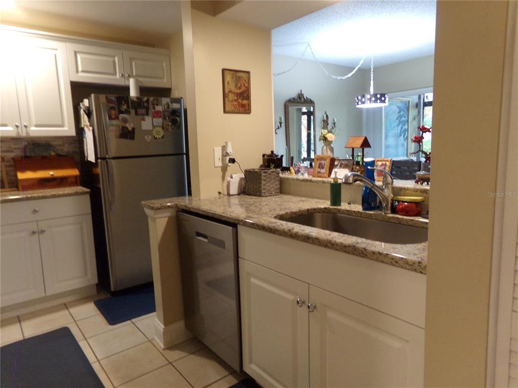 A kitchen features white cabinets, granite countertops, a stainless steel dishwasher, and a refrigerator — 110 CYPRESS WOODS CT UNIT 6A, DELTONA, FL