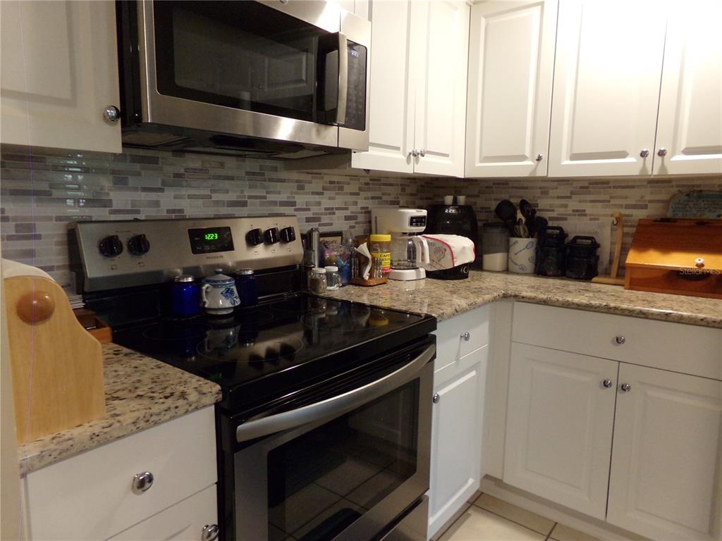 A kitchen features white cabinets, granite countertops, a stainless steel stove, and a tiled backsplash — 110 CYPRESS WOODS CT UNIT 6A, DELTONA, FL