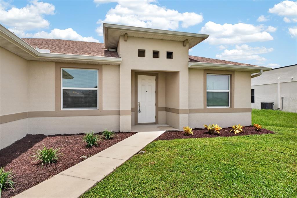 The exterior of a beige house features a white front door and a concrete walkway — 2714 NW 1ST PLACE, CAPE CORAL, FL