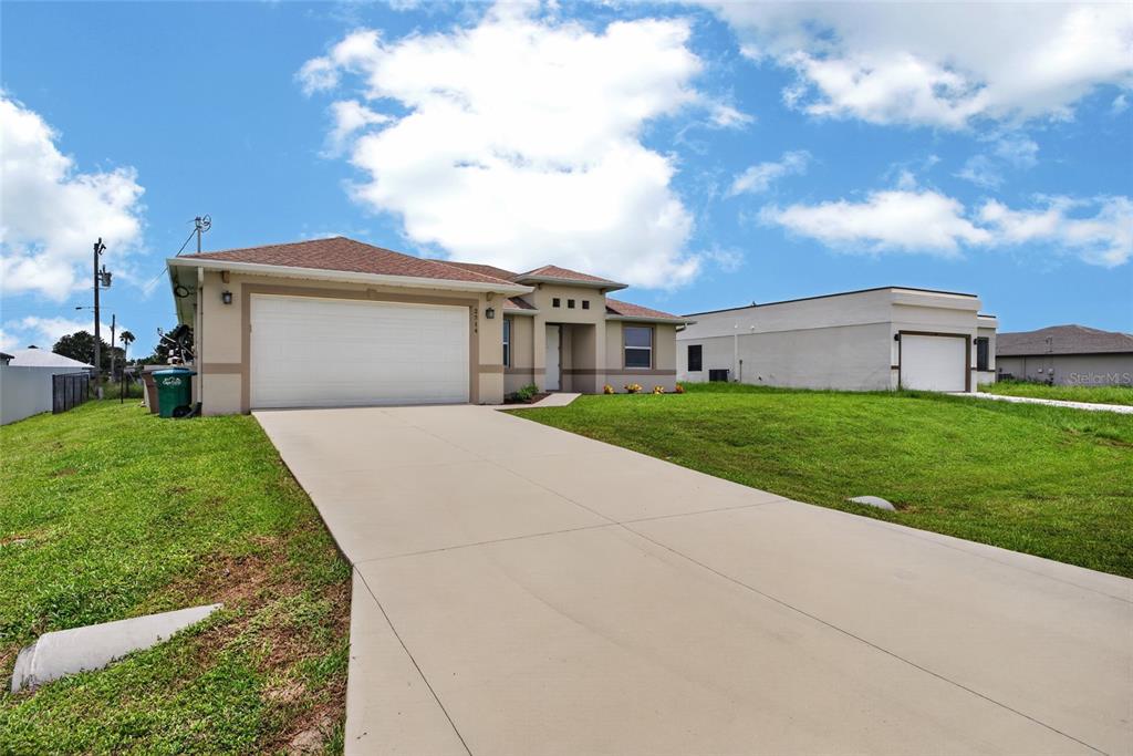 A single-story house with a two-car garage and a concrete driveway under a blue sky — 2714 NW 1ST PLACE, CAPE CORAL, FL