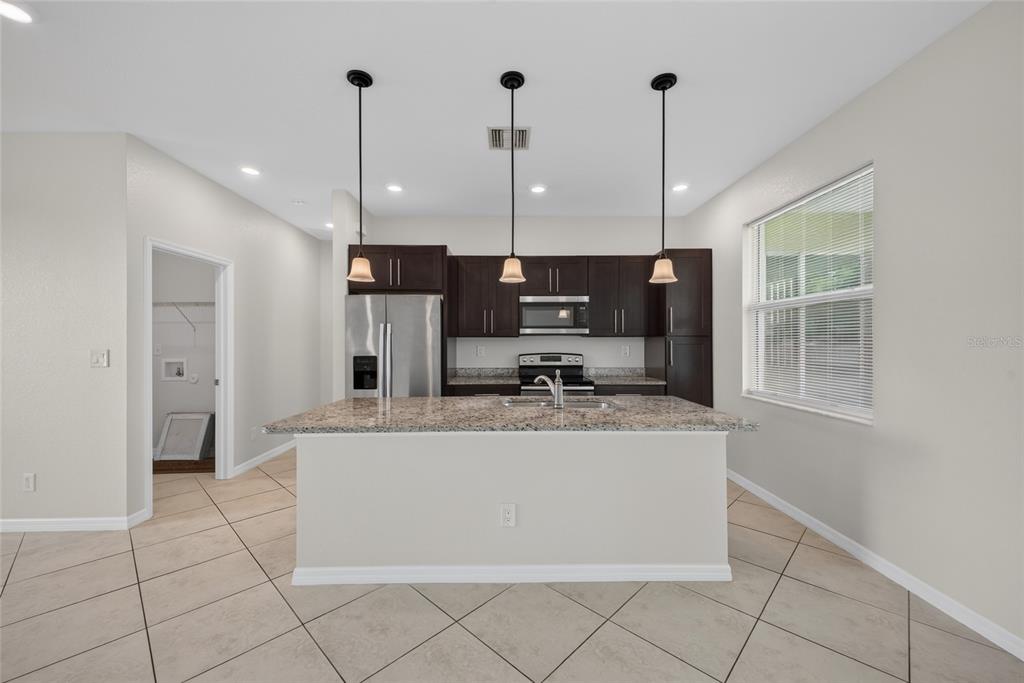 A kitchen features dark wood cabinets, granite countertops, a central island, and three pendant lights — 2714 NW 1ST PLACE, CAPE CORAL, FL